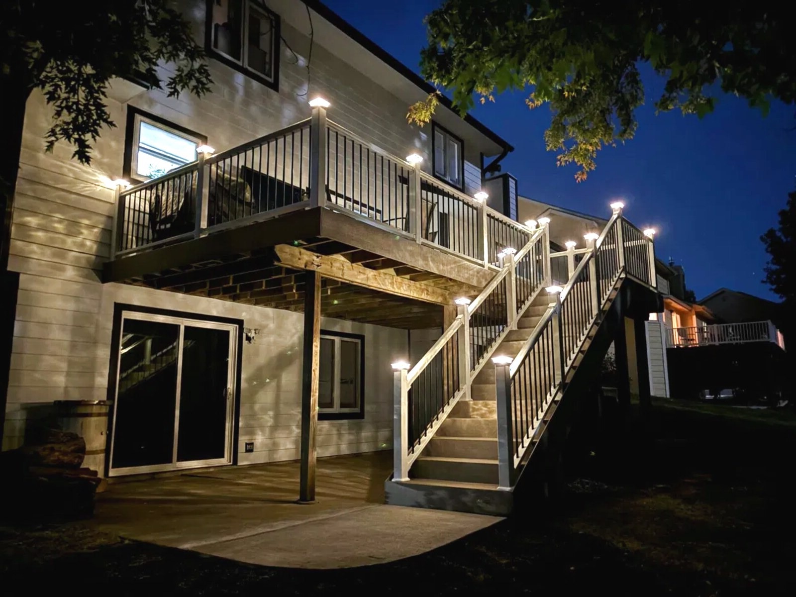 Two-story deck with lit stair railings and a covered patio beneath it at night